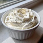 A close-up of fluffy, white horseradish sauce for prime rib, garnished with herbs, served in a small white ramekin.