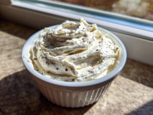 A close-up of freshly whipped horseradish sauce for prime rib, seasoned with dark specks, served in a white fluted ramekin near a window.