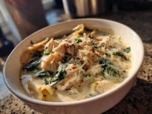 Close-up of a hearty bowl of white chicken lasagna soup, topped with shredded cheese and red pepper flakes.