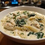 A close-up of a hearty bowl of white chicken lasagna soup with chunks of chicken, spinach, and pasta in a creamy sauce.