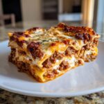 A thick, layered slice of rich meat lasagna topped with melted cheese and herbs, ready to eat.