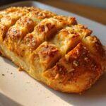 Close-up of a freshly baked, scored loaf of cheese bread topped with melted mozzarella and seasonings.