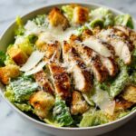 A close-up of a delicious chicken caesar salad with grilled chicken slices, croutons, and shaved parmesan cheese.