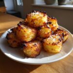 A pile of golden brown, incredibly crispy roast potatoes seasoned with sea salt, catching the sunlight.