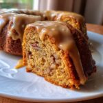 Close-up of a slice of moist apple dapple cake filled with pecans, topped with thick caramel glaze.