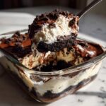 A spoonful of creamy Baileys Chocolate Cheesecake Trifle showing layers of white cream, dark chocolate cake, and chocolate sauce.
