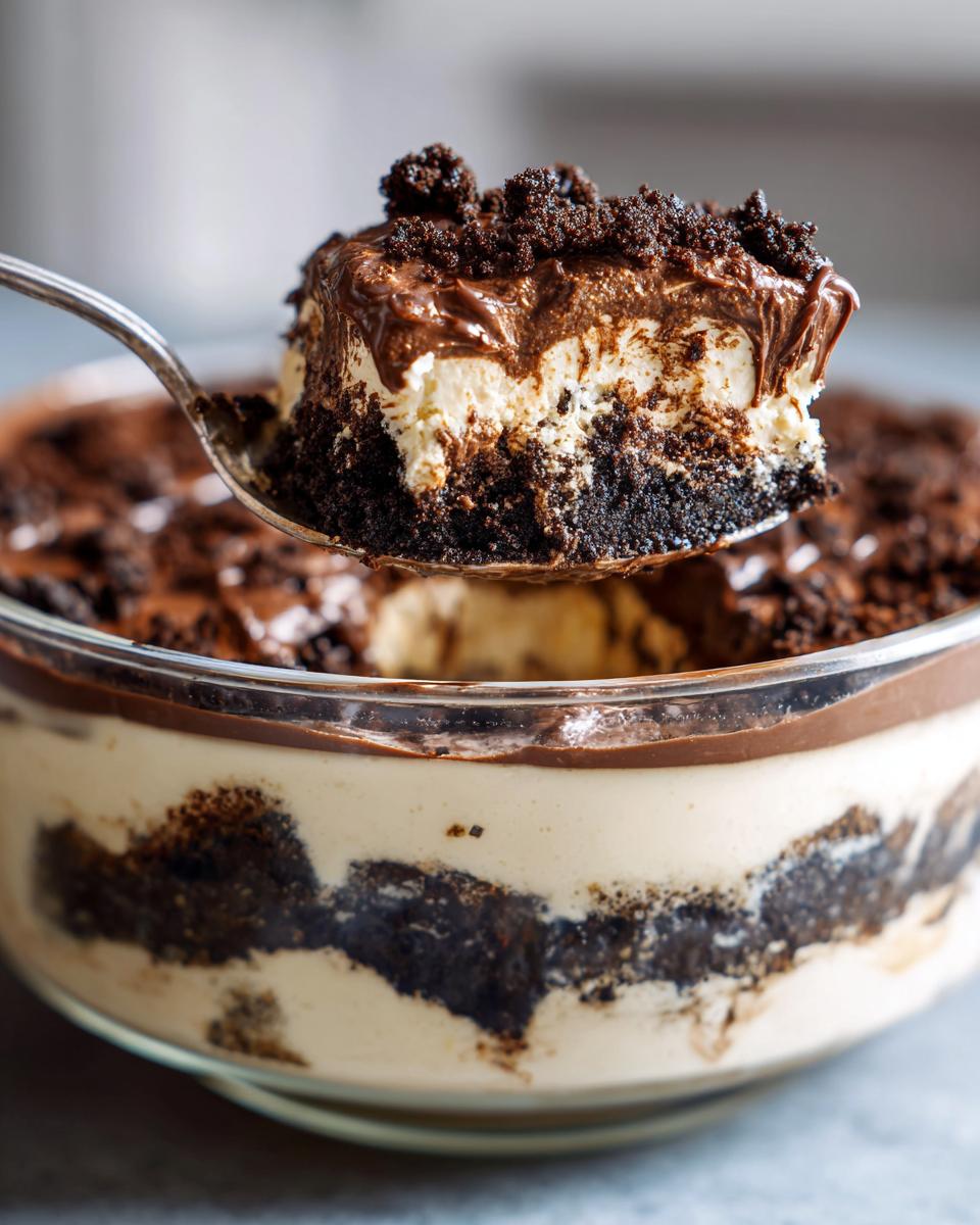 A spoonful of creamy Baileys Chocolate Cheesecake Trifle showing layers of chocolate crust, cream filling, and chocolate topping.