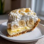 A decadent slice of banana cream pie featuring a graham cracker crust, thick custard, and topped with whipped cream and fresh banana slices.