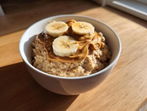 A white bowl filled with creamy banana oatmeal, topped generously with melted peanut butter and sliced bananas.