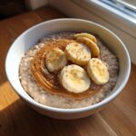 A bowl of creamy banana oatmeal topped with a swirl of peanut butter and fresh banana slices.