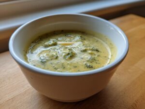 Close-up of a white bowl filled with creamy, yellow broccoli cheddar soup featuring visible florets.