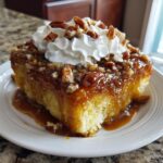 A decadent slice of butter pecan praline poke cake topped with caramel sauce, pecans, and whipped cream.