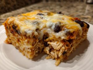 A square serving of cheesy chicken burrito bake, showing layers of rice, shredded chicken, black beans, and melted cheese topping.