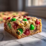 A close-up of a thick, chewy Christmas cookie bars square loaded with red and green M&M's.