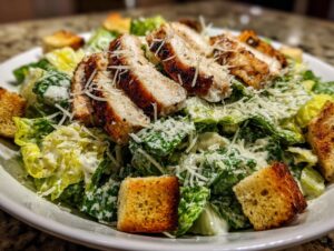 Close-up of a fresh chicken caesar salad topped with grilled chicken slices, croutons, and grated Parmesan cheese.