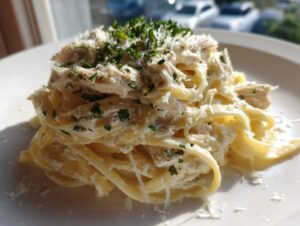 A close-up of a serving of creamy chicken fettuccine alfredo topped with grated Parmesan and fresh parsley.