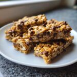 A stack of homemade no bake granola bars loaded with oats and chocolate chips on a white plate.