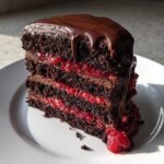 A decadent slice of chocolate raspberry cake with three layers of dark cake, raspberry filling, and chocolate ganache dripping down the side.
