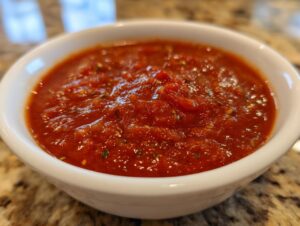 Close-up of a small white bowl filled with rich, chunky homemade tomato sauce, seasoned with herbs.