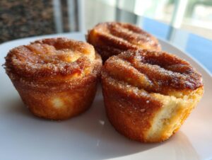 Close-up of three golden brown cinnamon sugar french toast muffins dusted heavily with sparkling cinnamon sugar.