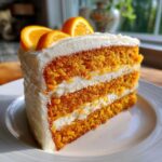 A tall slice of vibrant orange Creamsicle Cake layered with white frosting and topped with fresh orange slices.