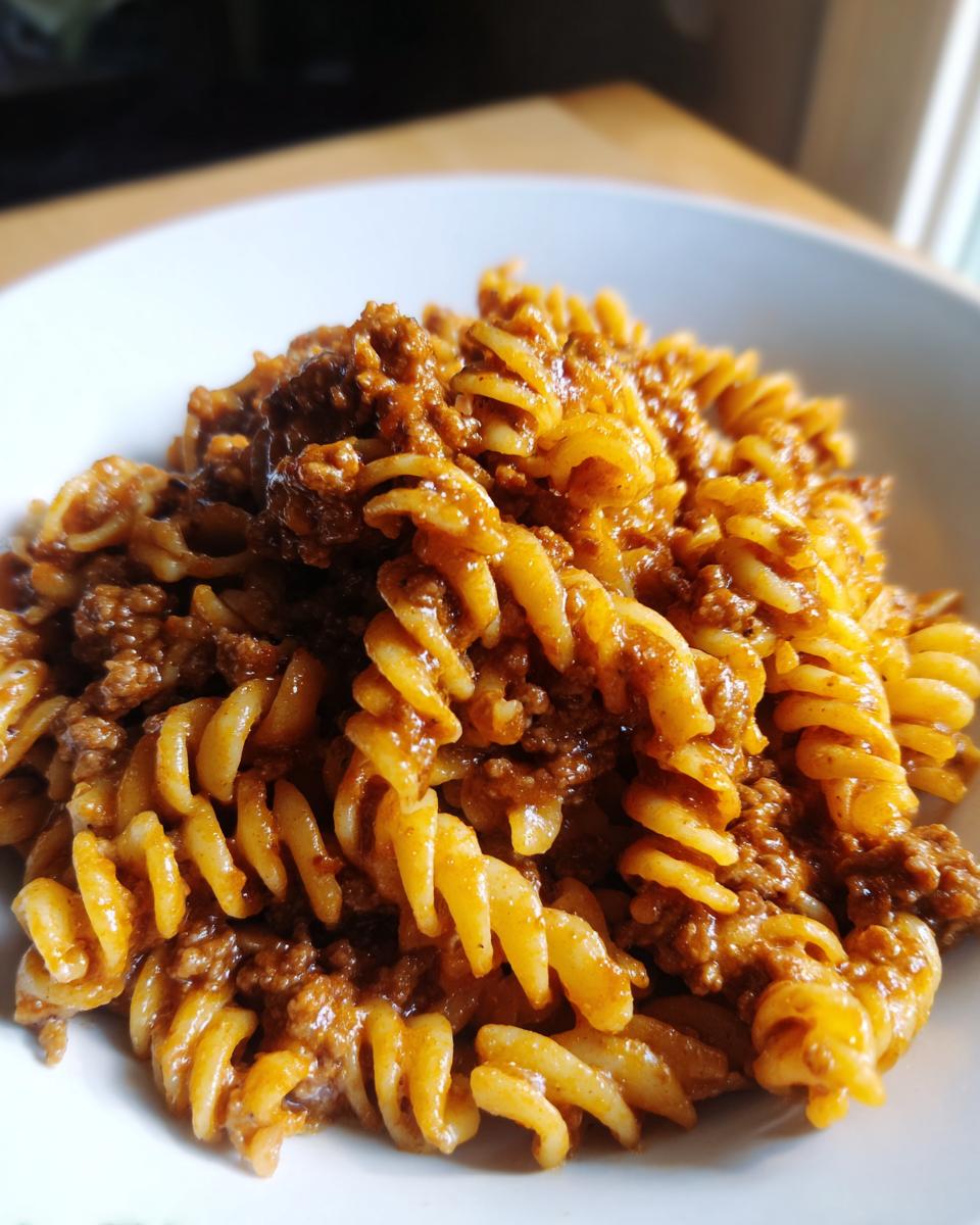 Close-up of a white bowl filled with creamy beef pasta made with fusilli noodles and a rich meat sauce.