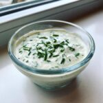Close-up of a creamy, white homemade salad dressing topped generously with fresh chopped chives.