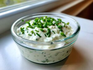 Close-up of a creamy, white homemade salad dressing topped generously with fresh chopped chives.