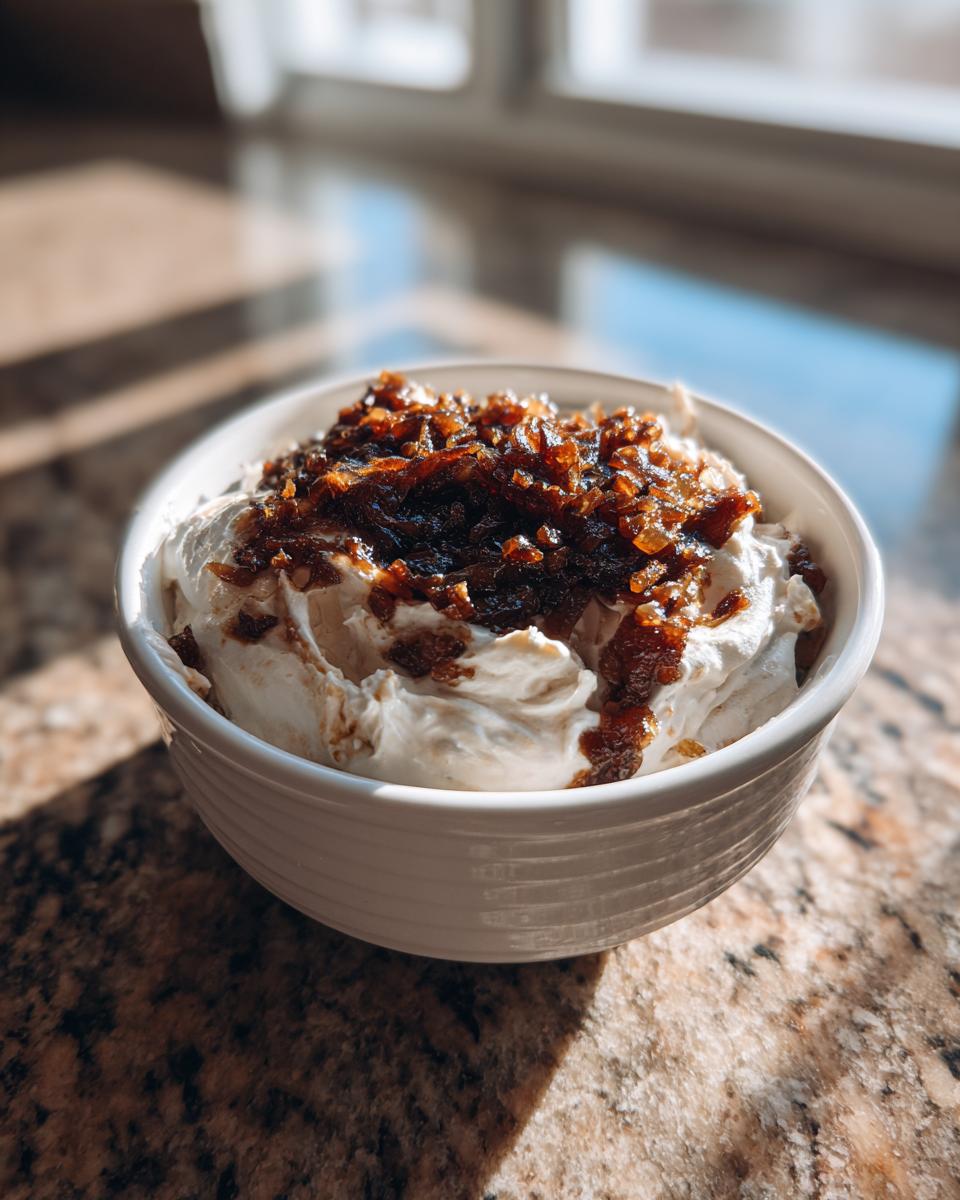 A white bowl filled with creamy onion dip, topped generously with dark caramelized onions.