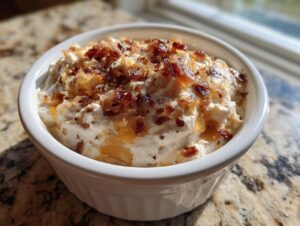 A white ramekin filled with creamy onion dip, generously topped with caramelized onions and bacon bits.