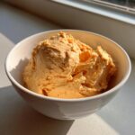 A close-up of creamy, orange pumpkin fluff served in a white bowl, highlighted by natural sunlight.