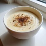 A close-up of creamy roasted cauliflower soup in a white bowl, topped with dark spices.