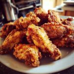 A close-up photo of a pile of crispy, golden-brown seasoned chicken wings served on a white plate.