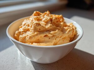 A close-up of light orange, airy pumpkin fluff dessert served in a white bowl.