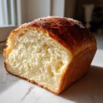 Close-up of a freshly baked condensed milk bread loaf, showing the soft, fluffy white interior and golden-brown crust.