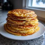 A tall stack of golden brown, fluffy pancakes served on a white plate.
