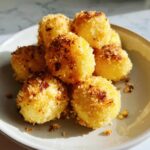 A pile of golden brown, breaded potato dumplings served on a light gray plate.