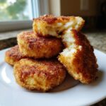 A stack of golden brown, crispy potato croquettes, one broken open showing the soft interior.