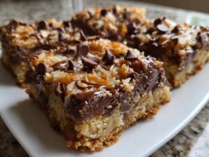 Close-up of gooey magic cookie bars topped with chocolate chips, coconut, and caramel drizzle.