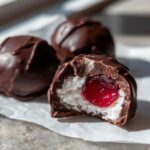 Close-up of a homemade chocolate covered cherries, showing the white coconut filling and bright red cherry center.
