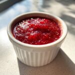 Close-up of bright red homemade cocktail sauce with visible texture in a small white ramekin.