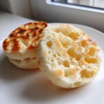 Close-up of a homemade english muffin, split open and drizzled with honey, showing its signature nooks and crannies.