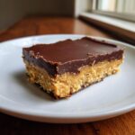 A single, decadent slice of peanut butter bars with a crumbly base, thick peanut butter filling, and smooth chocolate topping.