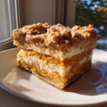 Two stacked squares of layered pumpkin crunch dessert with cream cheese filling and streusel topping.