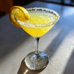 A vibrant yellow lemon drop martini in a coupe glass with a sugared rim and lemon twist garnish.