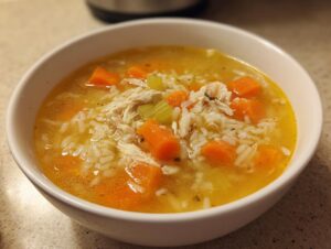 Close-up of a white bowl filled with Lemon Ginger Turmeric Chicken and Rice Soup, showing shredded chicken, rice, and diced carrots.
