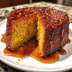 Close-up of a moist Bacardi Rum Cake with a thick, glossy caramel glaze dripping down the sides onto a white plate.