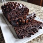 A sliced loaf of moist chocolate banana bread topped generously with melted chocolate chips on a white platter.
