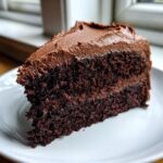 Close-up of a slice of moist chocolate cake layered with thick chocolate frosting.