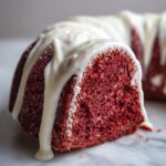 Close-up of a slice of moist red velvet bundt cake topped with thick, dripping white cream cheese glaze.